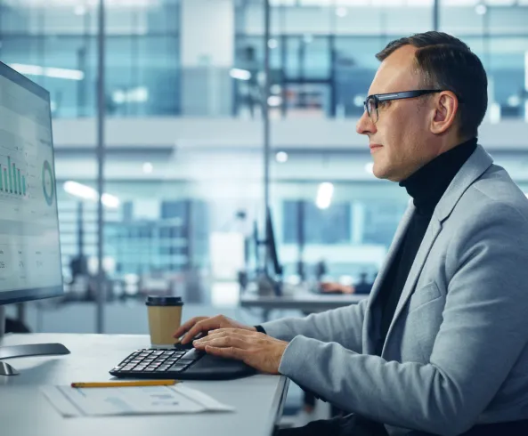 A man in business-casual attire analyzing data on a desktop computer