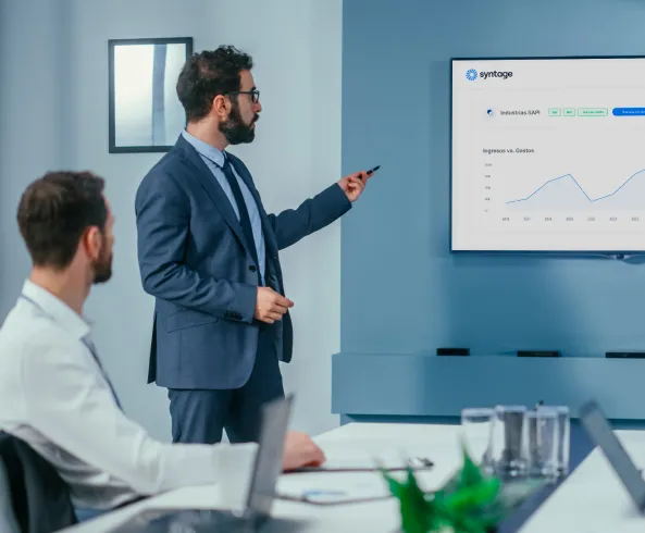 A person in a suit presenting data on a screen to another person in a boardroom